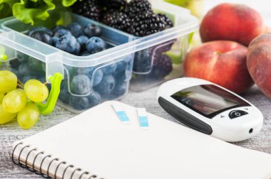 Kan şekeri ölçüm cihazı, boş defter ve çilek yemek kutusu ve meyve ve sebze ahşap tablo