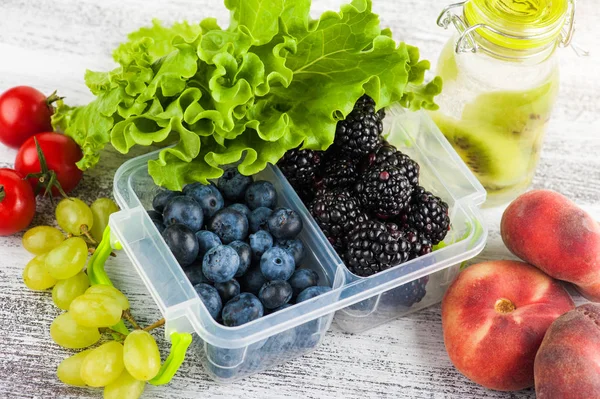 Berries in lunch box and fruits and vegetables on wooden table