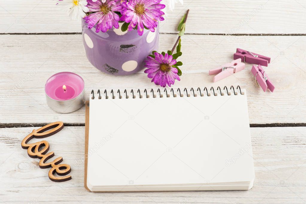 Empty notebook, lit candle and pink purple garden flowers on wooden background