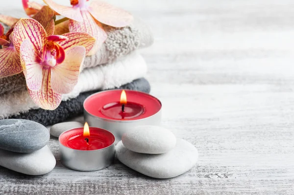 Spa still life with pebbles and red orange orchid, lit candle on wooden background