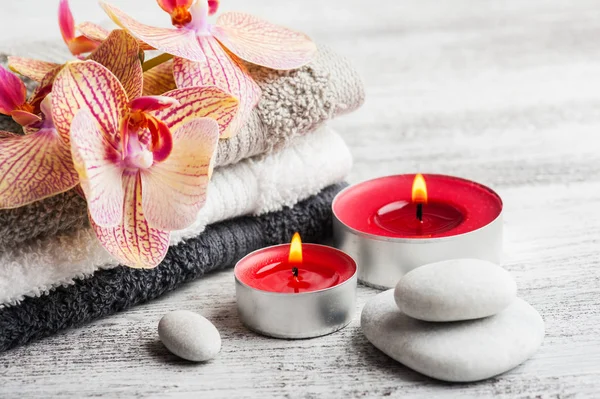 Spa still life with lit candles, pebbles and red orange orchid on wooden background