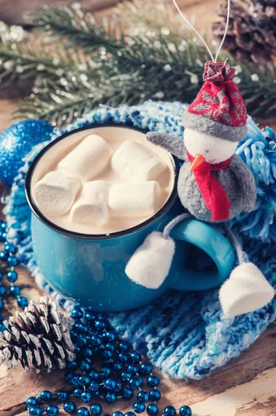 Blue mug of coffee with marshmallow and snowman, Christmas decor. Closeup on dark wooden background