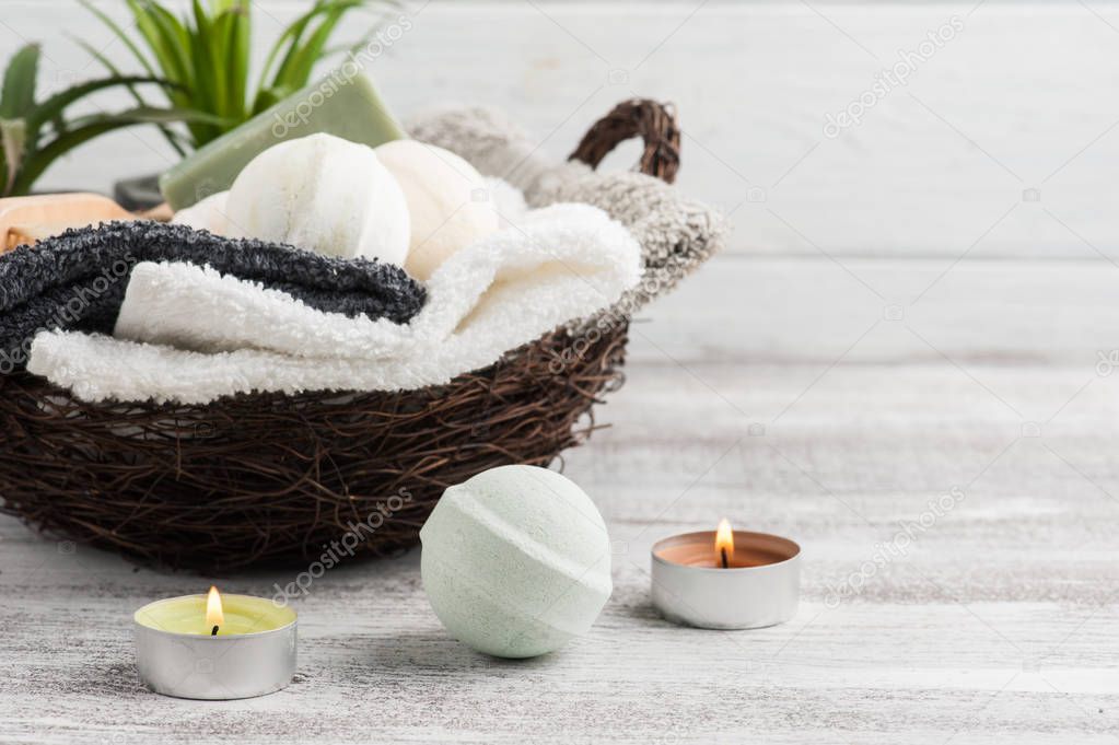 Folded towels in basket with bath bombs and lit candles. copy space