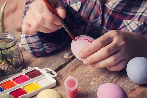 Femail hands holding paintbrush and easter egg, DIY composition on rustic wooden table