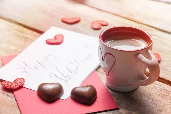 Cup of coffee and chocolate hearts, hand lettering happy valentine sign on rustic wooden table