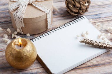 Boş bir defter, altın kuru çiçekler ve dekorasyon için yanan bir mum. Kraft hediyeli bir tatil ya da düğün organizatörü konsepti