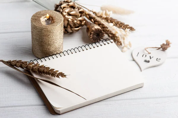 Boş bir defter, altın kuru çiçekler ve dekorasyon için yanan bir mum. Tatil ya da ahşap kalpli düğün organizatörü konsepti