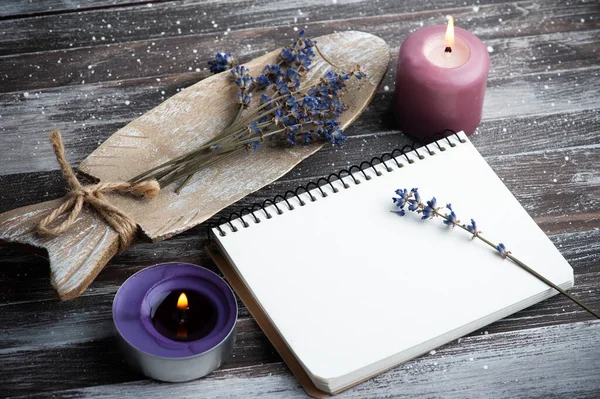Blank note book, purple aroma candles and dry lavender flowers on wooden rustic background. Summer or autumn set with copy space