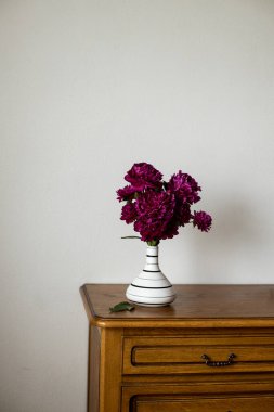 Siyah beyaz sürahi içinde koyu kahverengi oa üzerinde duran koyu pembe şakayık.