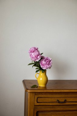 Koyu kahverengi meşe ağacının üstünde sarı bir sürahide duran pembe Peony.