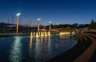 Çeşmelerin güzel gece manzarası, Ouchy, Lozan, İsviçre limanındaki sokak lambaları. Sudaki manzara ve yansıma.