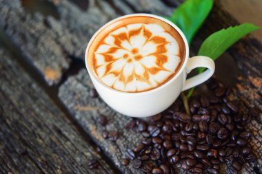 sıcak cappuccino ahşap masa / sıcak cappuccino kahve çekirdeği ve ahşap masa üzerinde yeşil yaprak ile