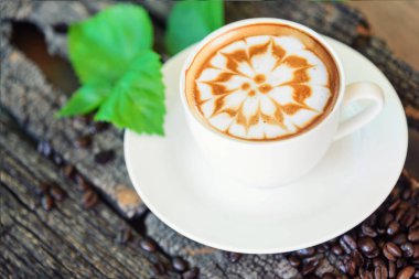 sıcak cappuccino ahşap masa / sıcak cappuccino kahve çekirdeği ve ahşap masa üzerinde yeşil yaprak ile