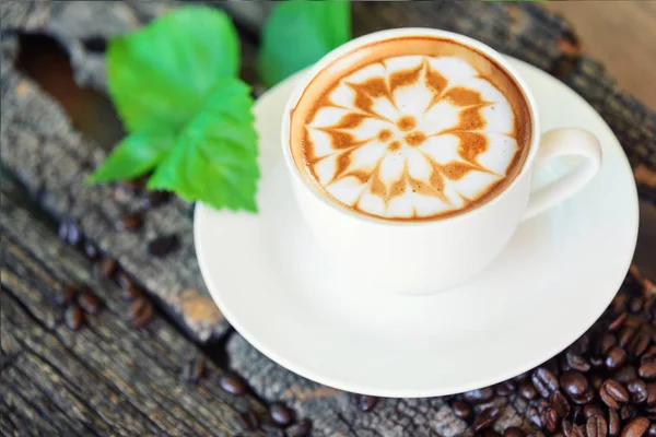 sıcak cappuccino ahşap masa / sıcak cappuccino kahve çekirdeği ve ahşap masa üzerinde yeşil yaprak ile