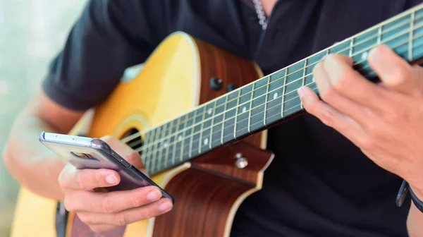 Gitarist akustik gitar zaman oynarken akıllı telefon kullanın