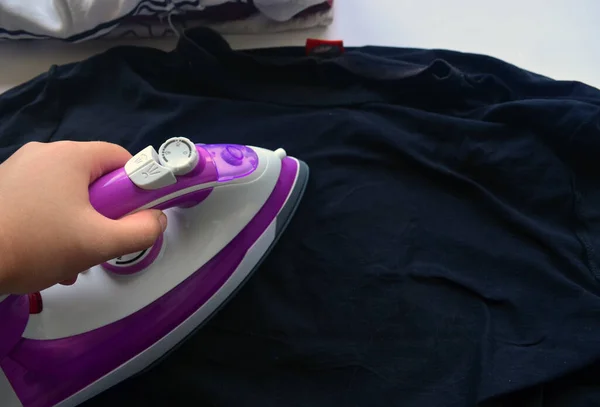 Çamaşır ütülemek için beyaz ve pembe ütü. Tişörtler, kazaklar, eşyalar. Ütü tahtası.