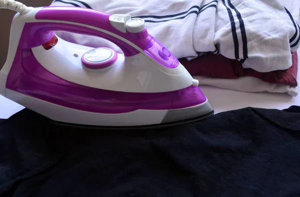 White and pink iron for ironing linen. T-shirts, sweaters, things. Ironing board.