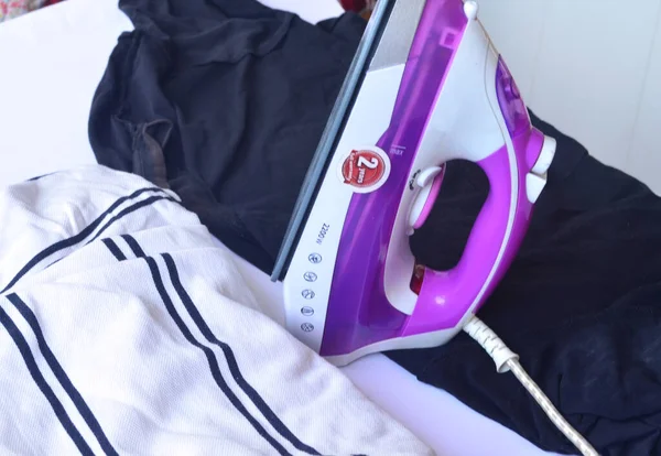 Çamaşır ütülemek için beyaz ve pembe ütü. Tişörtler, kazaklar, eşyalar. Ütü tahtası.