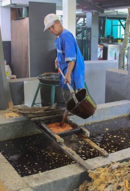 Yogyakarta, Java, Endonezya 'daki Batik Winotosastro fabrikasında çalışan bir işçi. Batik motifli beyaz kumaşı elle çizmek için balmumu ile çizim aracı kullanın