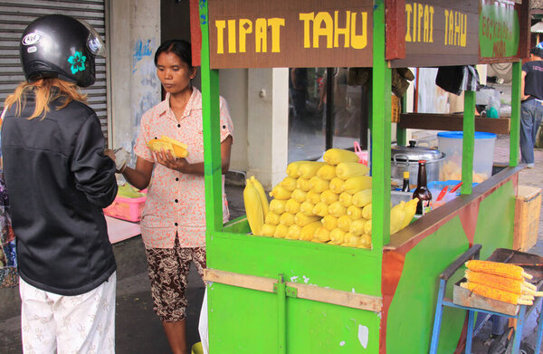 Tourist bargaining with steamed corn seller in the street, in Bali. Customer purchasing food from an indonesian street vendor. Street food vendors in Indonesia are almost everywhere.