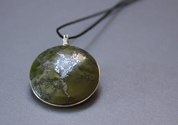 Single peruvian jade stone in handmade jewelry on grey background