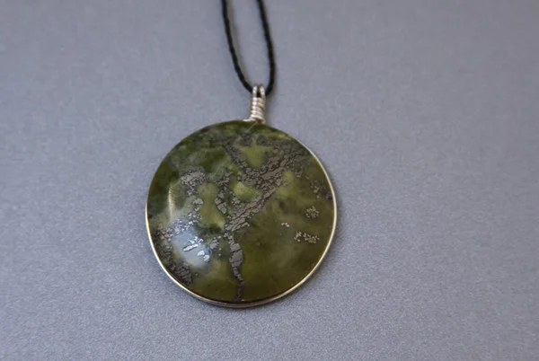 Single peruvian jade stone in handmade jewelry on grey background