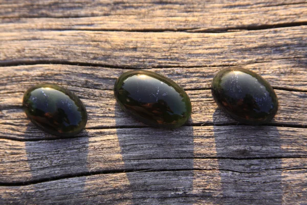 Black jade translucent green stone in sunlight on wood. The black jade is dark green in color, but under the light it is semi-transparent, appreciated by jewelers because the way it shines