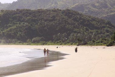 Mawun Beach Lombok 'ta el ele tutuşan bir çift ve scooter. Kuta Lombok Endonezya adasında egzotik bir cennettir. Güzel beyaz kumlu plajları ve kristal berrak turkuaz suları vardır..
