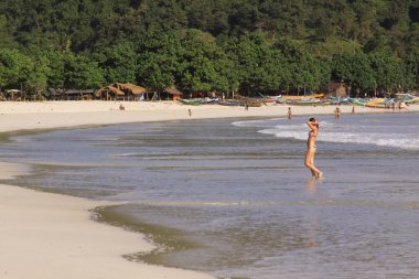 Kadın ve diğer insanlar, tropik sahilde, Mawun, Lombok. Kuta Lombok Endonezya adasında egzotik bir cennettir. Güzel beyaz kumlu plajları ve kristal berrak turkuaz suları vardır..