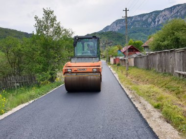 Romanya 'nın Transilvanya kentinin Apuseni köyündeki yeni inşa edilmiş köy yolunda asfalt pnömatik sıkıştırıcı. Sıcak asfaltı sıkıştıran vibratörlerin yol yapım prosedürü.