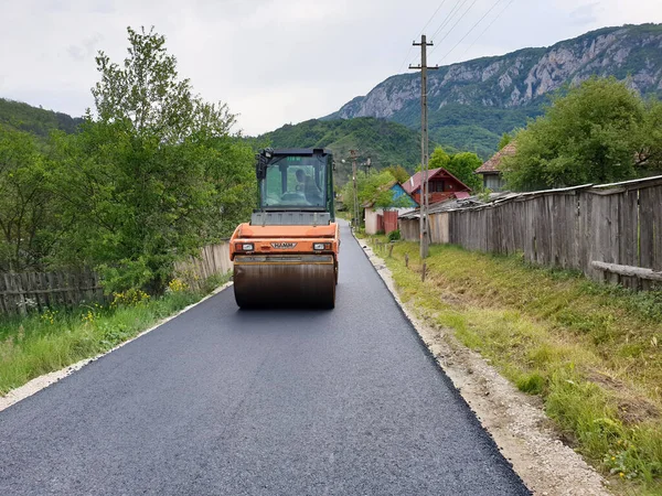 Romanya 'nın Transilvanya kentinin Apuseni köyündeki yeni inşa edilmiş köy yolunda asfalt pnömatik sıkıştırıcı. Sıcak asfaltı sıkıştıran vibratörlerin yol yapım prosedürü.