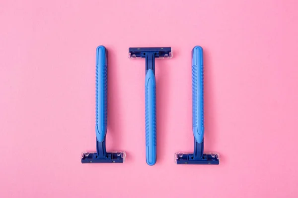 3 blue disposable razor blades on pink cardboard background