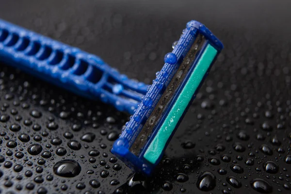 blue disposable razor blade, on black background with water drops