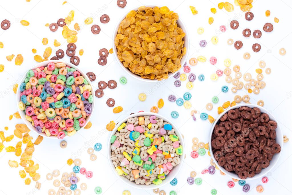 Four bowls of cereals and cereals scattered around the table on white background. A bowl of colored cereals, one of chocolate rings, one with cereals and marshmallow, and one with corn flex. Top view.