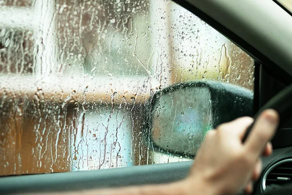 Drops of rain on the side window of the car, water falls from the driver\'s window. Bad weather concept. The driver is careful on the road