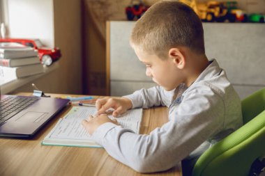 Çocuk ev ödevini evde yapar. Online eğitim. Adam kitaptaki çizgi boyunca parmağını hareket ettiriyor..