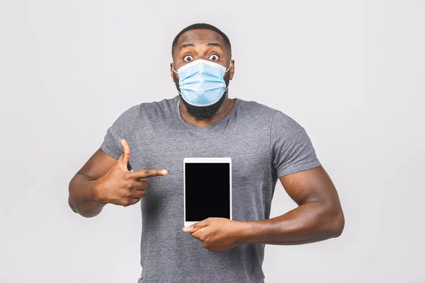 African american man with mask to protect him from Coronavirus. Corona virus pandemic. Person with medical mask. Isolated on white background. Holding tablet computer empty screen frame.