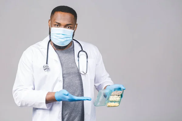 African american Doctor Showing Pills Wearing Gloves. Doctor Holding Tablets. Corona Virus Concept isolated over grey background.