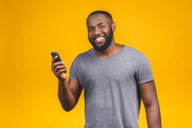 Yakışıklı, heyecanlı, neşeli, keyifli, sıradan giyinen meraklı adamın portresi ve sarı arka planda izole edilmiş sevgilisine mesajlar ulaştırması. Telefon kullanılıyor. 