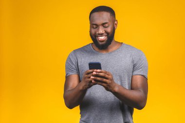 Yakışıklı, heyecanlı, neşeli, keyifli, sıradan giyinen meraklı adamın portresi ve sarı arka planda izole edilmiş sevgilisine mesajlar ulaştırması. Telefon kullanılıyor. 