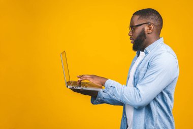 Sarı arka planda izole edilmiş dizüstü bilgisayar kullanan ciddi bir Afrikalı Amerikalı..