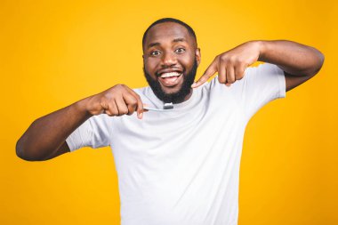 Diş fırçalı bir adam. Diş fırçasıyla diş fırçası tutan ve sarı arka planda duran genç, üstsüz Afrikalı bir adamın resmi..