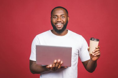Heyecanlı mutlu Afro-Amerikalı adam, bilgisayar ekranı, kahve ya da çay ile kırmızı arka planda izole edilmiş zaferi kutluyor.. 