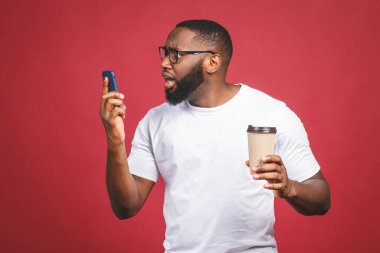Cep telefonu olan ve kahve fincanını götüren afro-amerikalı bir adamın portresi. Kırmızı arkaplan üzerinde izole edilmiş.