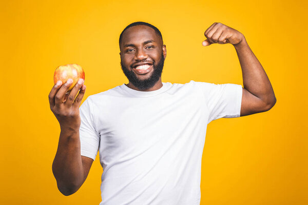 Healthy african american man holding an apple isolated against yellow background. 