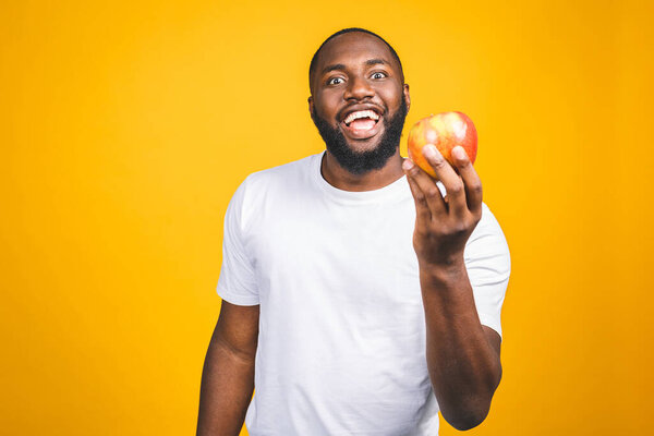 Healthy african american man holding an apple isolated against yellow background. 