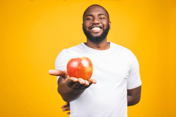 Healthy african american man holding an apple isolated against yellow background. 