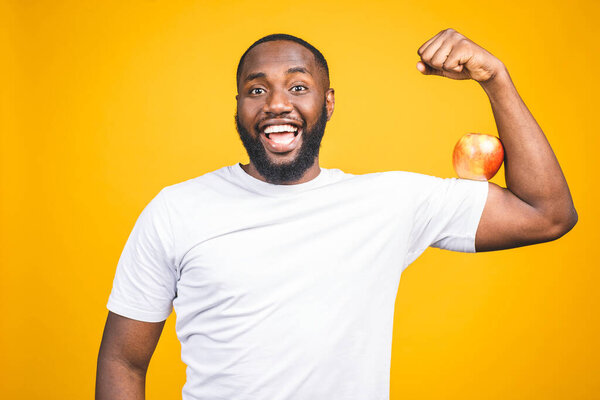 Healthy african american man holding an apple isolated against yellow background. 