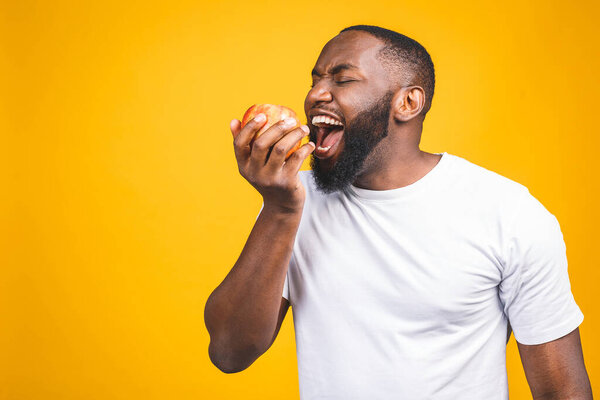 Healthy african american man holding an apple isolated against yellow background. 