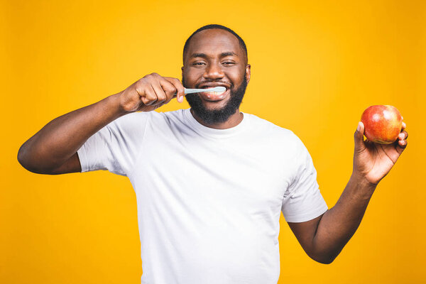Man with tooth brush. Image of young shirtless African man holding a toothbrush with toothpaste and apple, smiling while standing against yellow background.